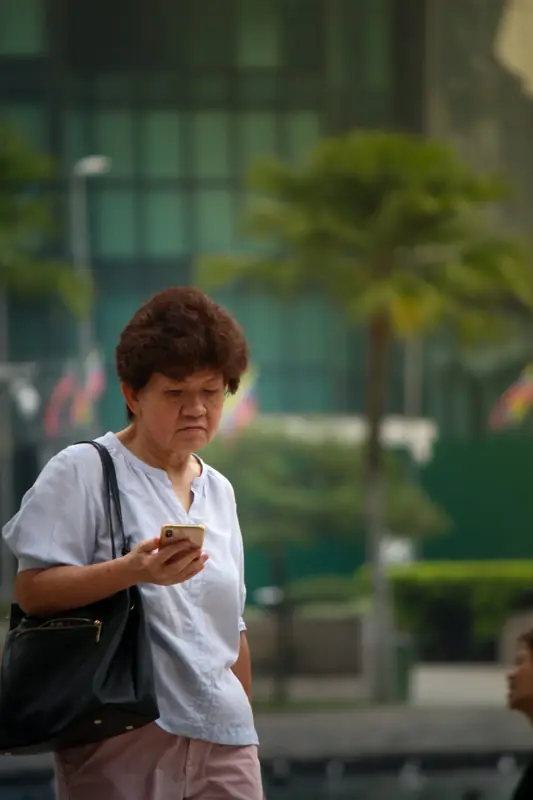 An older Asian woman checking her phone on the street