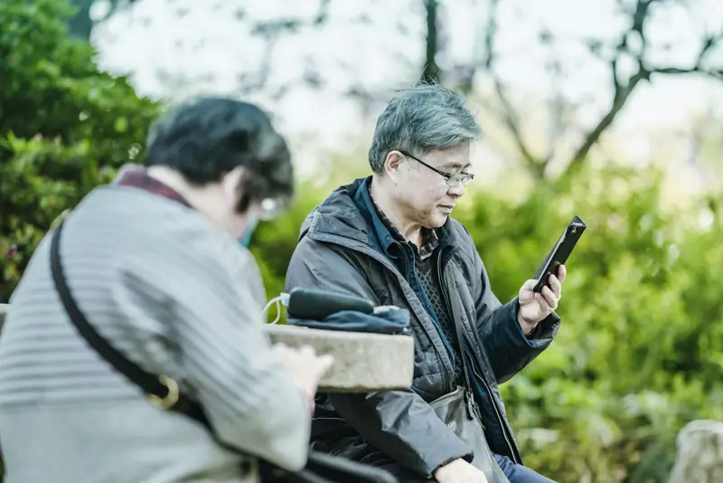 Two older Asian adults looking at their phones in a park